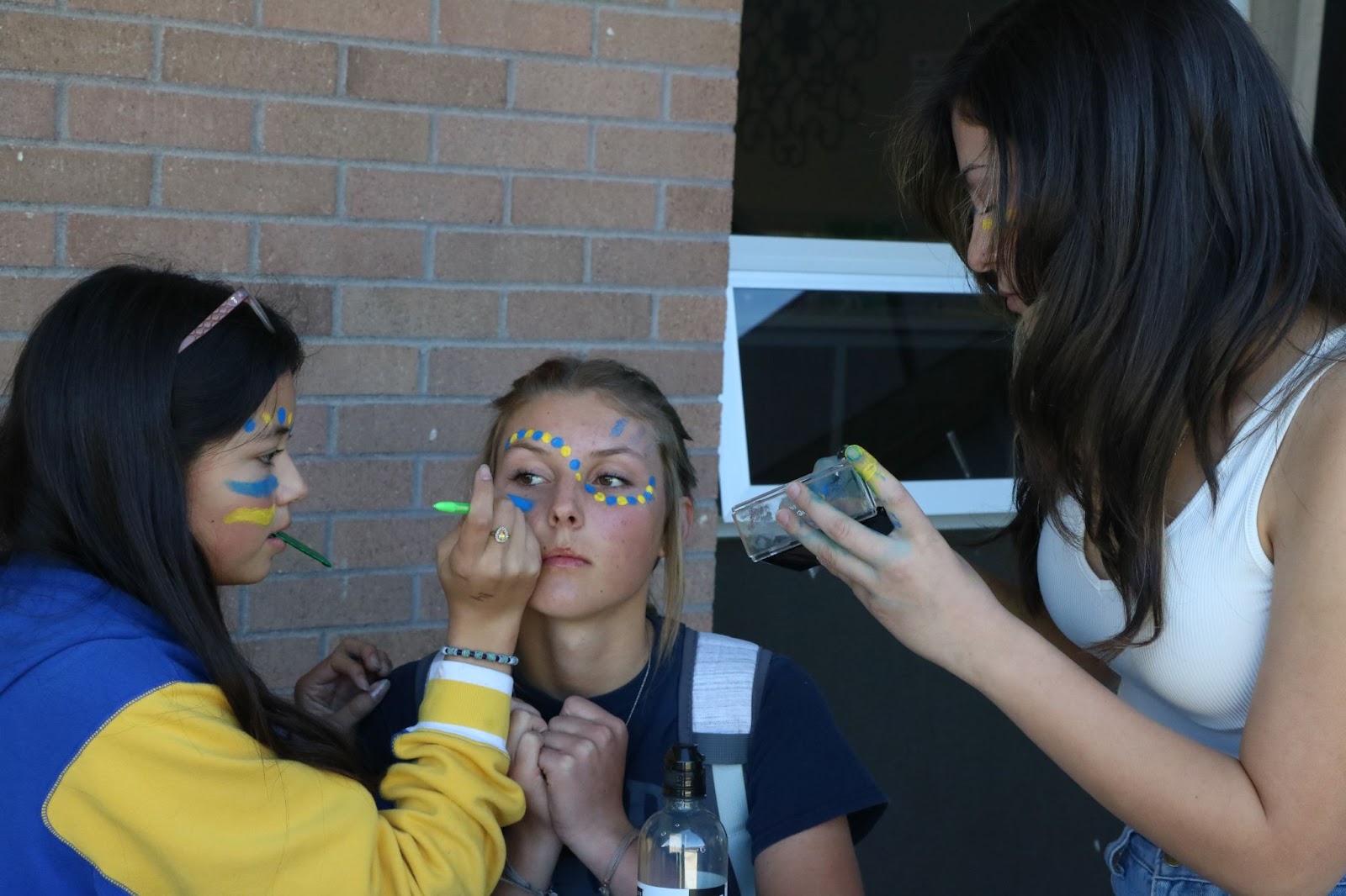 Freshmen Maria Palacios, Yocelyn Perez and Audry Mason show their participation on Blue and Gold Day through festive face painting. /Lainey Novacek • The Brand