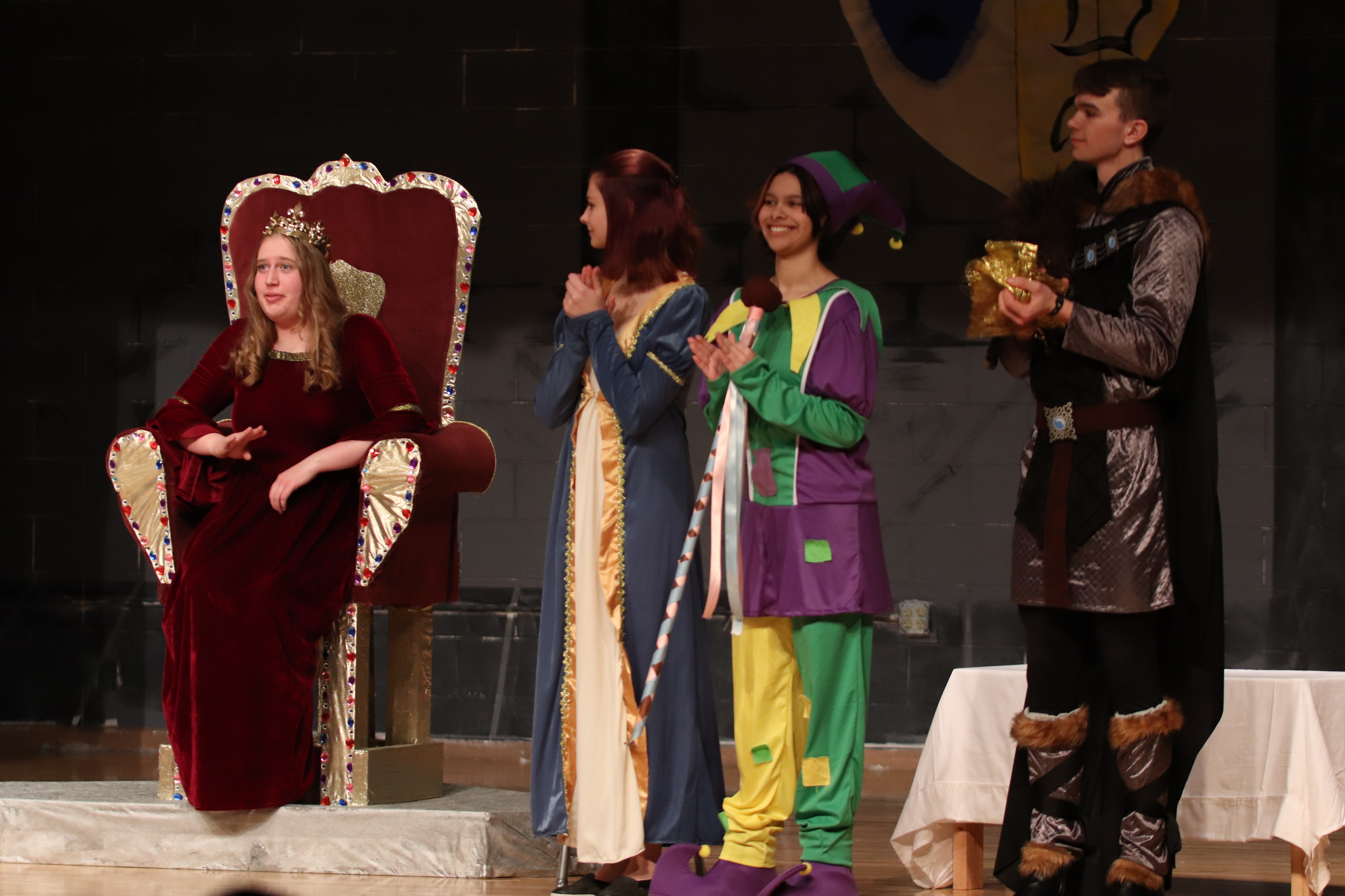 The Queen played by Kaylee Radtke, says something and Morgan Rorex as Lady Matilda, Sage Huerta as the Jester, and Joseph Vankuiken as the Huntsman all applaud in agreement and praise. /Jovi Anderson • The Brand